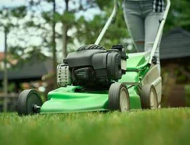 A person mowing a lawn with a green lawn mower