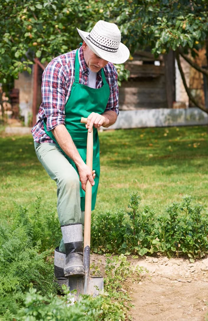 A man pressing a shovel to the ground with his feet